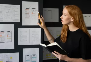 Designers analisando prot&oacute;tipos de aplicativos m&oacute;veis para desenvolvimento de produto em uma parede com sketches e wireframes.