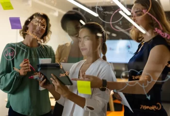 Equipe de profissionais de marketing colaborando e gerenciando estrat&eacute;gias em uma reuni&atilde;o de gest&atilde;o de equipes de marketing com uso de dispositivos digitais.
