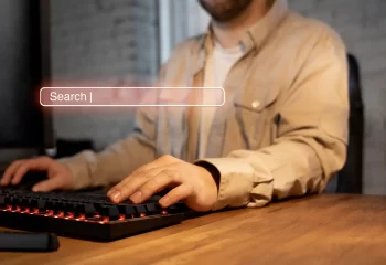 Pessoa usando teclado de computador com uma busca online, representando a import&acirc;ncia da autoridade t&oacute;pica no SEO na era da intelig&ecirc;ncia artificial.